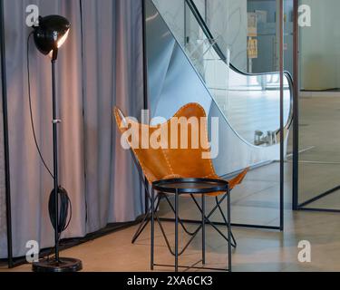 Una sedia in pelle posizionata vicino a un tavolo accanto a una lampada Foto Stock