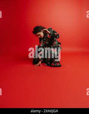 Una donna alla moda che posa contro un muro rosso vibrante Foto Stock