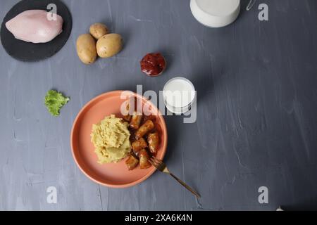 Cena di cucina: Purè di patate, salsicce, salsicce, latte, ketchup e materie prime, tuberi, patate, pollo, insalata su sfondo grigio con spa Foto Stock