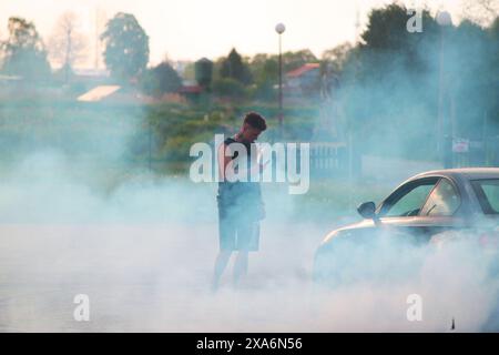 Un giovane che fotografa un'auto fumante con il suo cellulare. Foto Stock