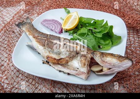 Vista dall'alto del pesce di spigola su una griglia. Spigola grigliata. Mare al forno. Branzino grigliato servito su un piatto con varie salse e decorato con parsl Foto Stock