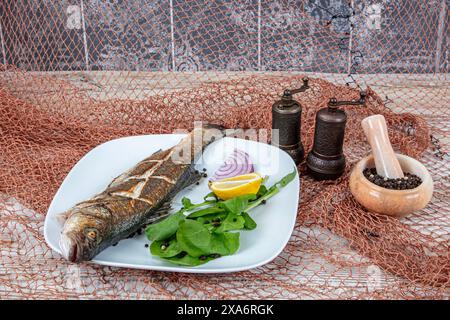 Vista dall'alto del pesce di spigola su una griglia. Spigola grigliata. Mare al forno. Branzino grigliato servito su un piatto con varie salse e decorato con parsl Foto Stock