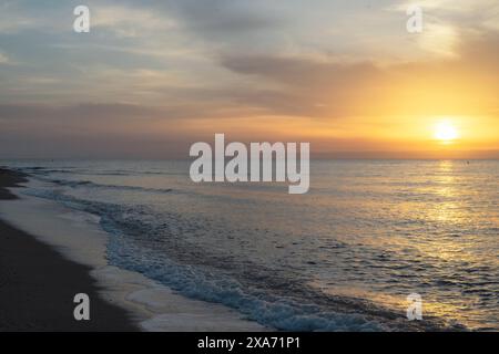 All'alba, l'oceano è tranquillo, il cielo è un'arancia vibrante e il sole sbircia attraverso le nuvole. Foto Stock