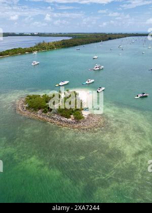 Diverse barche ancorate in acque turchesi cristalline vicino a una spiaggia con isole e alberi lussureggianti Foto Stock