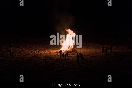 le persone si riuniscono intorno a un falò in un campo rurale (calore invernale, famiglia che festeggia insieme) fuoco alto, fiamma, caldo (di notte con il freddo) Foto Stock