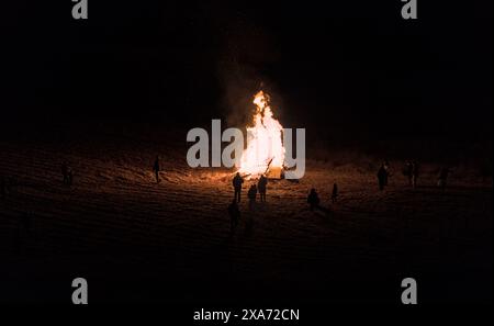 le persone si riuniscono intorno a un falò in un campo rurale (calore invernale, famiglia che festeggia insieme) fuoco alto, fiamma, caldo (di notte con il freddo) Foto Stock