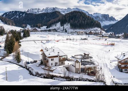 Paesaggio innevato a Selva di Val Gardena, incastonato tra torreggianti montagne dolomitiche, con edifici bianchi visibili Foto Stock