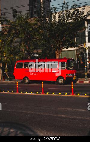 Un autobus rosso attraversa una strada della città, passando davanti agli edifici Foto Stock