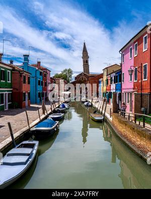 Un fiume attraversa una città rurale con case colorate nelle vicinanze e barche in un canale Foto Stock