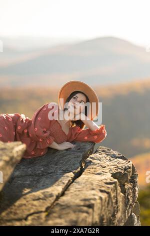 Una donna con un cappello da sole sdraiata sul bordo di una roccia Foto Stock
