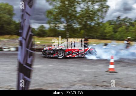 Una persona che guida un'auto da corsa rossa, bianca e nera su un circuito speedway Foto Stock