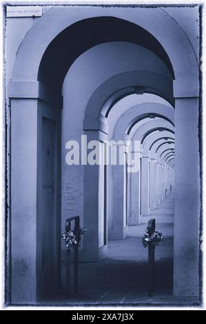 Una vecchia fotografia di un corridoio con file di colonne e sedie, due non occupate Foto Stock