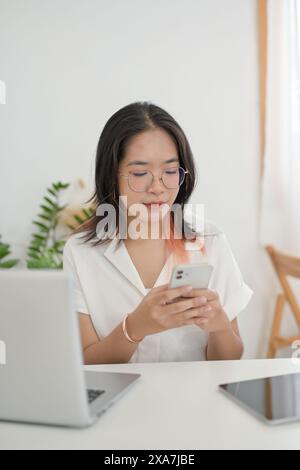Una giovane donna asiatica sta controllando i messaggi o rispondendo alla chat sul suo smartphone mentre lavora in remoto da un bar. concetto di persone e tecnologia wireless Foto Stock