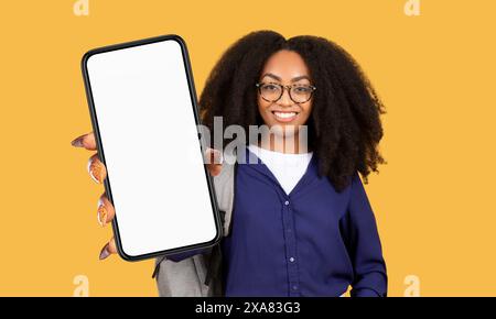 Donna con occhiali che regge lo smartphone davanti allo sfondo giallo Foto Stock