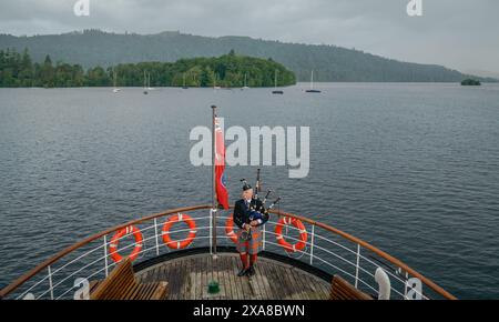 Il solitario Richard Cowie, dei massoni della Cumbria, gioca sul ponte di una delle crociere sul lago Windermere, i tradizionali piroscafi a Bowness-on-Windermere, Lake District, durante un evento commemorativo del D-Day. Il Pifferaio ha giocato in varie località della Cumbria meridionale negli ultimi 8 giorni, per onorare il pifferaio del D-Day Bill Millin che ha giocato sulle spiagge della Normandia il D-Day per confondere le truppe nemiche e aumentare il morale delle truppe alleate. Data foto: Mercoledì 5 giugno 2024. Foto Stock