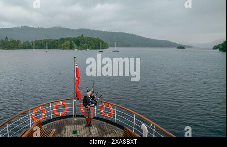 Il solitario Richard Cowie, dei massoni della Cumbria, gioca sul ponte di una delle crociere sul lago Windermere, i tradizionali piroscafi a Bowness-on-Windermere, Lake District, durante un evento commemorativo del D-Day. Il Pifferaio ha giocato in varie località della Cumbria meridionale negli ultimi 8 giorni, per onorare il pifferaio del D-Day Bill Millin che ha giocato sulle spiagge della Normandia il D-Day per confondere le truppe nemiche e aumentare il morale delle truppe alleate. Data foto: Mercoledì 5 giugno 2024. Foto Stock