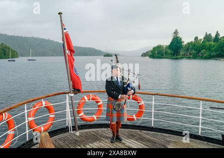 Il solitario Richard Cowie, dei massoni della Cumbria, gioca sul ponte di una delle crociere sul lago Windermere, i tradizionali piroscafi a Bowness-on-Windermere, Lake District, durante un evento commemorativo del D-Day. Il Pifferaio ha giocato in varie località della Cumbria meridionale negli ultimi 8 giorni, per onorare il pifferaio del D-Day Bill Millin che ha giocato sulle spiagge della Normandia il D-Day per confondere le truppe nemiche e aumentare il morale delle truppe alleate. Data foto: Mercoledì 5 giugno 2024. Foto Stock