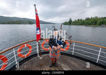 Il solitario Richard Cowie, dei massoni della Cumbria, gioca sul ponte di una delle crociere sul lago Windermere, i tradizionali piroscafi a Bowness-on-Windermere, Lake District, durante un evento commemorativo del D-Day. Il Pifferaio ha giocato in varie località della Cumbria meridionale negli ultimi 8 giorni, per onorare il pifferaio del D-Day Bill Millin che ha giocato sulle spiagge della Normandia il D-Day per confondere le truppe nemiche e aumentare il morale delle truppe alleate. Data foto: Mercoledì 5 giugno 2024. Foto Stock