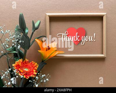 Messaggio di ringraziamento con fiori e cuore in cornice di legno su sfondo marrone Foto Stock