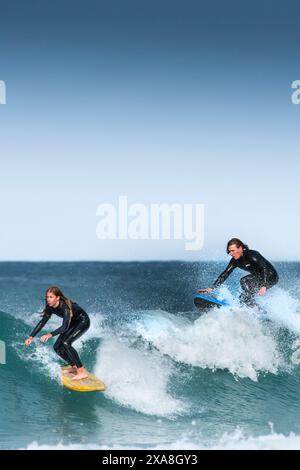 Due surfisti che cavalcano un'onda al Fistral di Newquay in Cornovaglia nel Regno Unito. Foto Stock