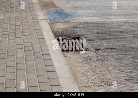 Un sistema di drenaggio sul lato di una strada in cui l'acqua fuoriesce, importante per la manutenzione della superficie stradale e per prevenire le inondazioni Foto Stock