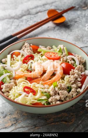Insalata tailandese con spaghetti istantanei, gamberi, maiale macinato e verdure da vicino in un recipiente sul tavolo. Verticale Foto Stock