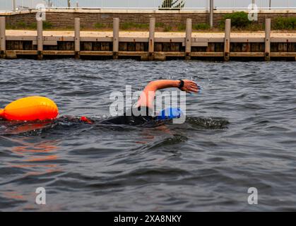 Una donna che nuota in mare aperto vicino alla riva indossando una boa di sicurezza e una muta nera. Foto Stock