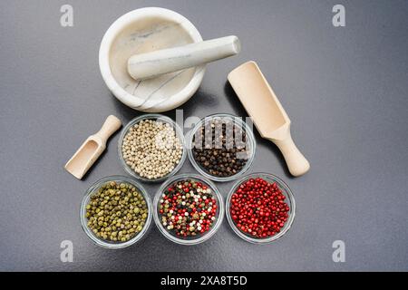 Mix di pepe rosso, nero, bianco e verde in ciotole di vetro con pala di legno e mortaio Foto Stock