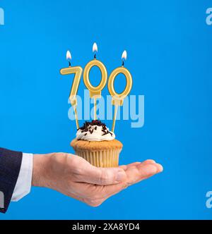 Cupcake per il compleanno a mano - candela numero 700 su sfondo blu Foto Stock