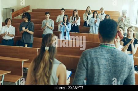 Due insegnanti, conferenze che conducono workshop per gruppi di studenti multirazziali. Ragazzi e ragazze in piedi in classe a battere le mani Foto Stock