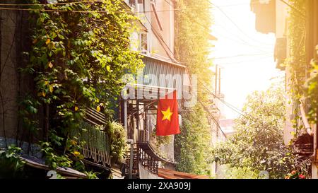 Una vibrante bandiera nazionale vietnamita rossa ondeggia in modo prominente su un balcone di una casa, in via della città di Hanoi, simboleggiando l'orgoglio nazionale e l'unità in mezzo a te Foto Stock