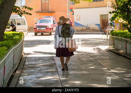 Donna boliviana tradizionale che cammina attraverso una piazza pubblica in un villag Foto Stock