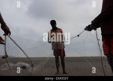 5 giugno 2024, Cox's Bazar, Chittagong, Bangladesh: Pescatori che preparano le reti da pesca per pescare il pesce sulla spiaggia di Cox's Bazar, Bangladesh. Il sostentamento della comunità dei pescatori dipende in larga misura dalla pesca. Con ogni nodo e regolazione, onorano una tradizione senza tempo di sostentamento che si armonizza con i ritmi del mondo naturale. Cox's Bazar, la spiaggia marina naturale più lunga del mondo, si estende per oltre 120 chilometri lungo la costa sud-orientale del Bangladesh. Rinomato per le sue sabbie dorate, i vivaci tramonti e il surf ondulato, attrae milioni di turisti ogni anno. (Immagine di credito: © Joy Foto Stock