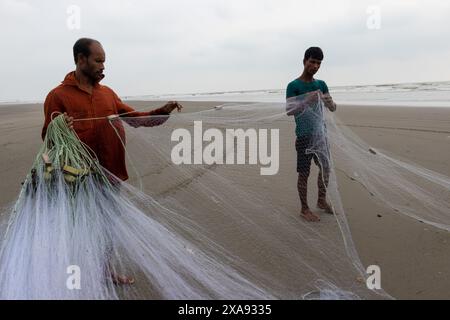 5 giugno 2024, Cox's Bazar, Chittagong, Bangladesh: Pescatori che preparano le reti da pesca per pescare il pesce sulla spiaggia di Cox's Bazar, Bangladesh. Il sostentamento della comunità dei pescatori dipende in larga misura dalla pesca. Con ogni nodo e regolazione, onorano una tradizione senza tempo di sostentamento che si armonizza con i ritmi del mondo naturale. Cox's Bazar, la spiaggia marina naturale più lunga del mondo, si estende per oltre 120 chilometri lungo la costa sud-orientale del Bangladesh. Rinomato per le sue sabbie dorate, i vivaci tramonti e il surf ondulato, attrae milioni di turisti ogni anno. (Immagine di credito: © Joy Foto Stock