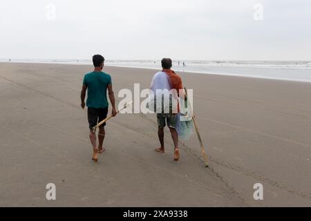 5 giugno 2024, Cox's Bazar, Chittagong, Bangladesh: Pescatori che preparano le reti da pesca per pescare il pesce sulla spiaggia di Cox's Bazar, Bangladesh. Il sostentamento della comunità dei pescatori dipende in larga misura dalla pesca. Con ogni nodo e regolazione, onorano una tradizione senza tempo di sostentamento che si armonizza con i ritmi del mondo naturale. Cox's Bazar, la spiaggia marina naturale più lunga del mondo, si estende per oltre 120 chilometri lungo la costa sud-orientale del Bangladesh. Rinomato per le sue sabbie dorate, i vivaci tramonti e il surf ondulato, attrae milioni di turisti ogni anno. (Immagine di credito: © Joy Foto Stock