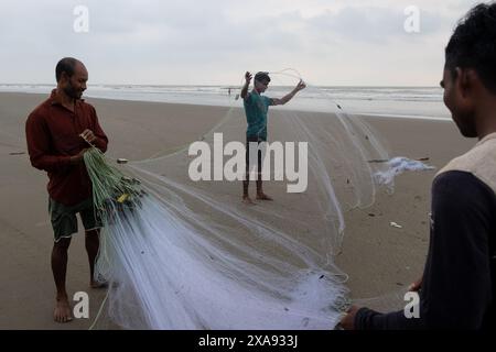 5 giugno 2024, Cox's Bazar, Chittagong, Bangladesh: Pescatori che preparano le reti da pesca per pescare il pesce sulla spiaggia di Cox's Bazar, Bangladesh. Il sostentamento della comunità dei pescatori dipende in larga misura dalla pesca. Con ogni nodo e regolazione, onorano una tradizione senza tempo di sostentamento che si armonizza con i ritmi del mondo naturale. Cox's Bazar, la spiaggia marina naturale più lunga del mondo, si estende per oltre 120 chilometri lungo la costa sud-orientale del Bangladesh. Rinomato per le sue sabbie dorate, i vivaci tramonti e il surf ondulato, attrae milioni di turisti ogni anno. (Immagine di credito: © Joy Foto Stock