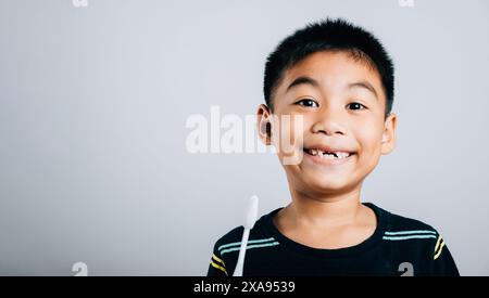 Isolato su uno sfondo bianco, un ragazzo asiatico senza denti superiori a latte tiene uno spazzolino da denti Foto Stock