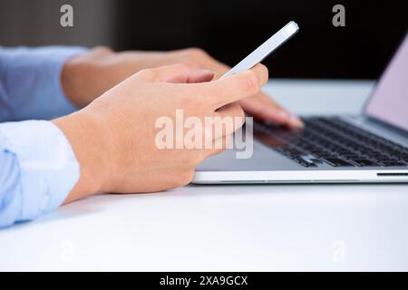Ripresa laterale delle mani di una donna con smartphone e computer portatile Foto Stock