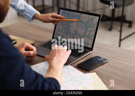 Cartografi che lavorano con una mappa catastale su un computer portatile al tavolo di legno in ufficio, primo piano Foto Stock