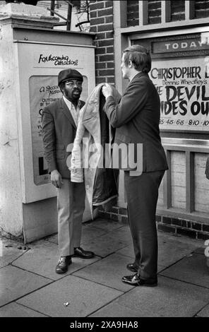 Le leggi SUS, permettevano alla polizia di fermarsi e cercare qualsiasi "persona sospettata" in qualsiasi momento. Un afro Caribbean Black British viene fermato e perquisito da un semplice detective vestito. Il detective non ha supporto per lui. Notting Hill, Londra, Inghilterra anni '1972 1970 UK HOMER SYKES Foto Stock