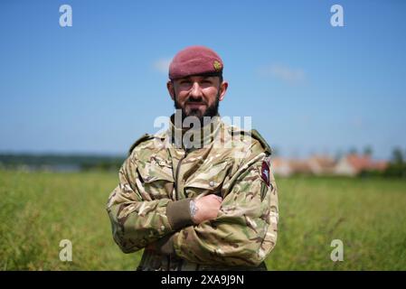 Il capitano Maik Biggs, del 16 Medical Regiment, il cui nonno ha combattuto per i nazisti nella seconda guerra mondiale, si pone dopo aver partecipato a un salto con paracadute accanto ai membri delle forze armate britanniche, belghe, canadesi e statunitensi, organizzato dalla Royal Air Force e dall'esercito britannico sulla "zona di lancio K", vicino a Sannerville, in Francia, per commemorare il ruolo delle forze aviotrasportate durante gli sbarchi in Normandia, in vista del 80° anniversario del D-Day. Data foto: Mercoledì 5 giugno 2024. Foto Stock