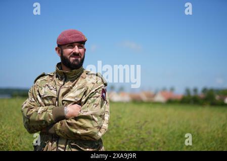 Il capitano Maik Biggs, del 16 Medical Regiment, il cui nonno ha combattuto per i nazisti nella seconda guerra mondiale, si pone dopo aver partecipato a un salto con paracadute accanto ai membri delle forze armate britanniche, belghe, canadesi e statunitensi, organizzato dalla Royal Air Force e dall'esercito britannico sulla "zona di lancio K", vicino a Sannerville, in Francia, per commemorare il ruolo delle forze aviotrasportate durante gli sbarchi in Normandia, in vista del 80° anniversario del D-Day. Data foto: Mercoledì 5 giugno 2024. Foto Stock