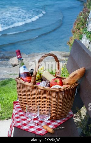 Cestino da picnic in vimini con prodotti francesi, tra cui vino rosato, baguette uva saucisson, vista sul paesaggio, onde, mare, Bretagna, Francia Foto Stock