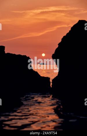 Il sole si stende sopra le rocce di una spiaggia, riflettendo nell'acqua Foto Stock