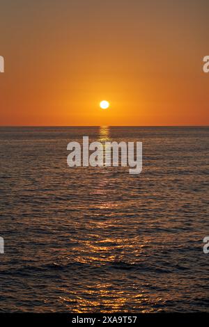 Il sole tramonta sull'oceano da una spiaggia di sabbia Foto Stock