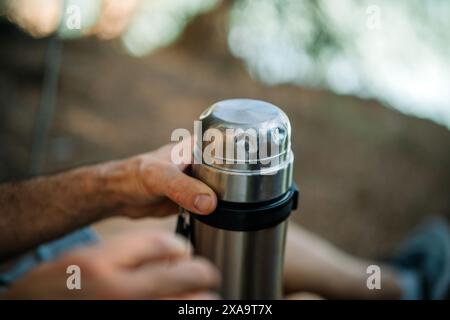 Un uomo seduto a terra che tiene una bottiglia d'acqua vicino a un'altra mano Foto Stock