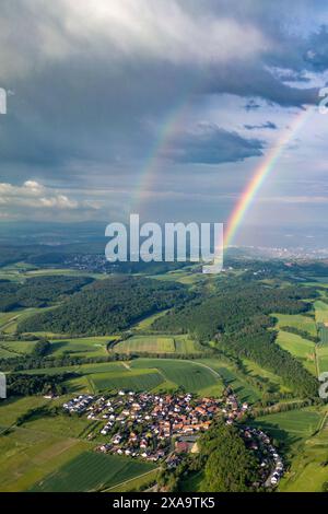 Una vista aerea del doppio arcobaleno sulle montagne con il piccolo villaggio in primo piano Foto Stock