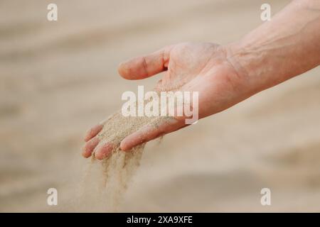La mano di un uomo che versa sabbia nel deserto del Qatar Foto Stock