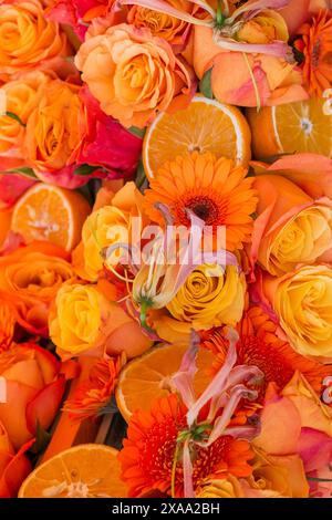 Un'arancia vibrante e rose rosa disposte con fiori assortiti in bouquet Foto Stock