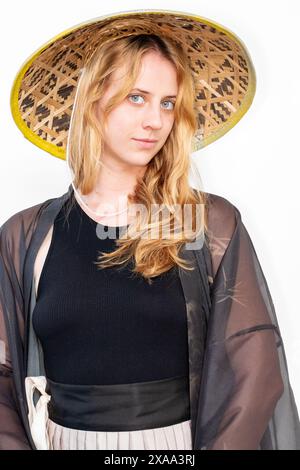 Una cosplayer donna in una veste con maniche trasparenti e un cappello asiatico in posa su uno sfondo bianco Foto Stock